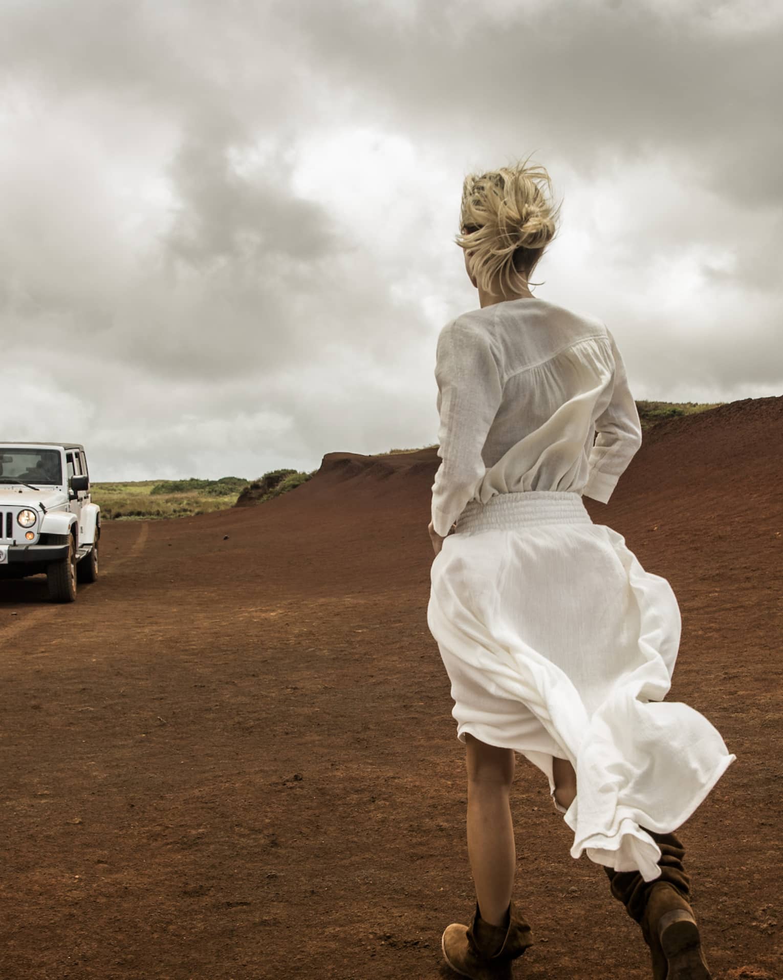 A white jeep approaches a woman on a windy day